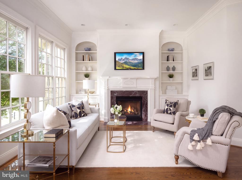 Living room with tall windows, a white fireplace, built-in shelves, and upholstered seating.