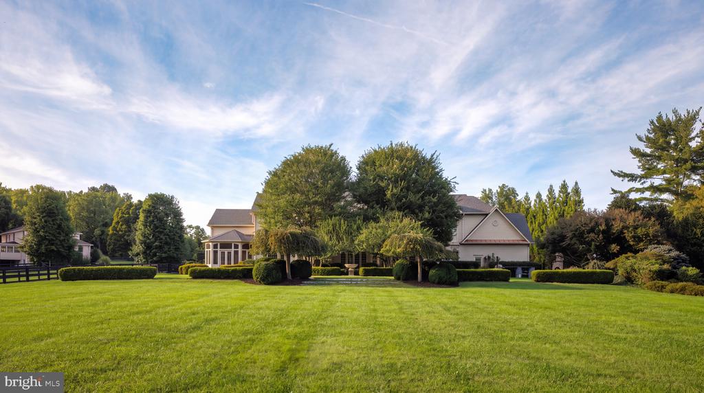Large house behind mature trees, with a broad manicured lawn and clipped shrubs.