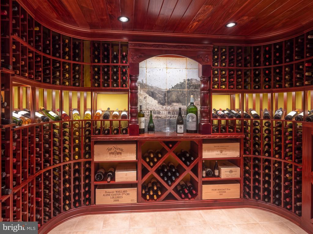 Wine cellar with curved red wood cabinetry, bottle racks, and a stone mural framed by a carved arch.