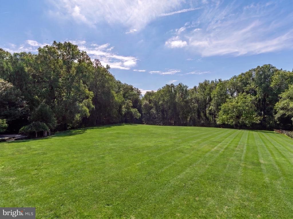 Expansive striped lawn bordered by mature trees beneath a partly cloudy sky.