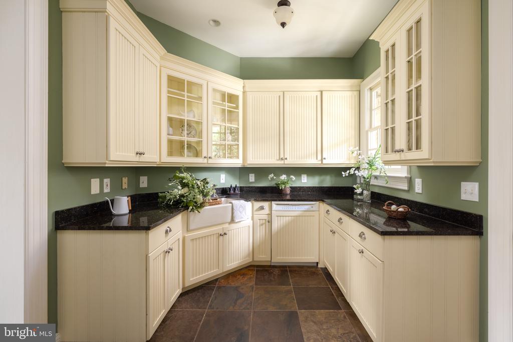 U-shaped kitchen with cream cabinets, dark granite counters, sage-green walls, and a farmhouse sink.