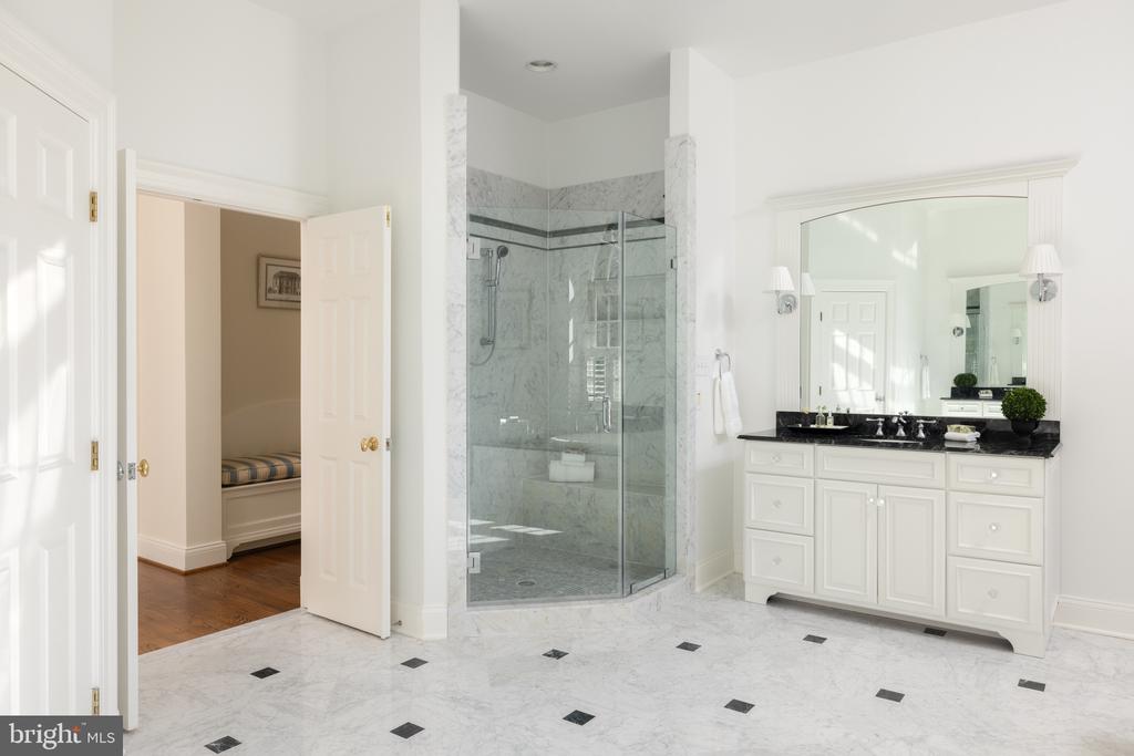 Bright bathroom with a glass-enclosed marble shower, black vanity countertop, and marble floor.