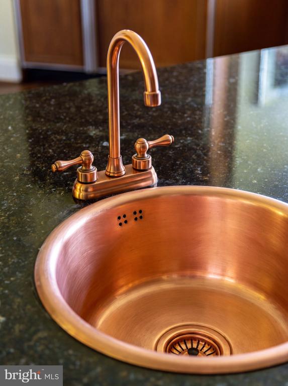 Copper kitchen sink and faucet set into a dark granite countertop.