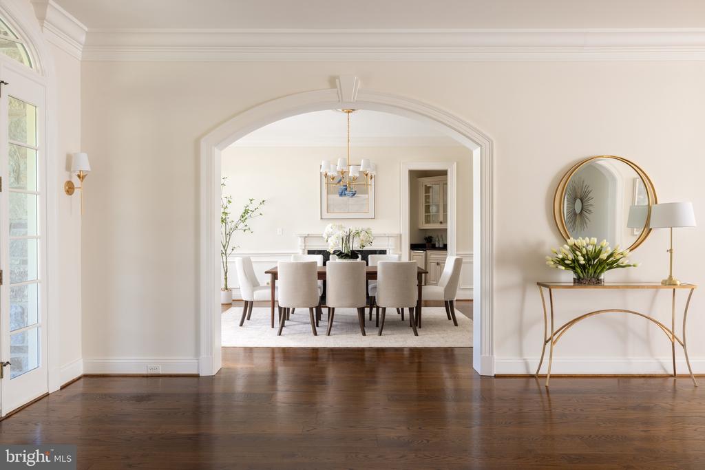 Furnished dining room framed by a broad archway, with a dark wood table and chandelier.