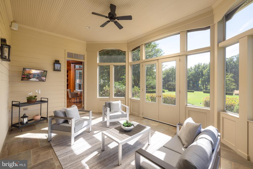 Furnished sunroom with expansive windows overlooking a green lawn and garden.