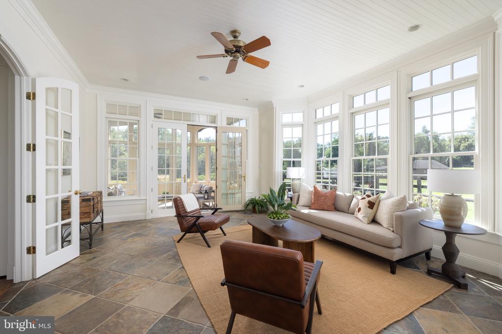 Bright sunroom with white-framed windows, tiled floor, and neutral seating around a coffee table.