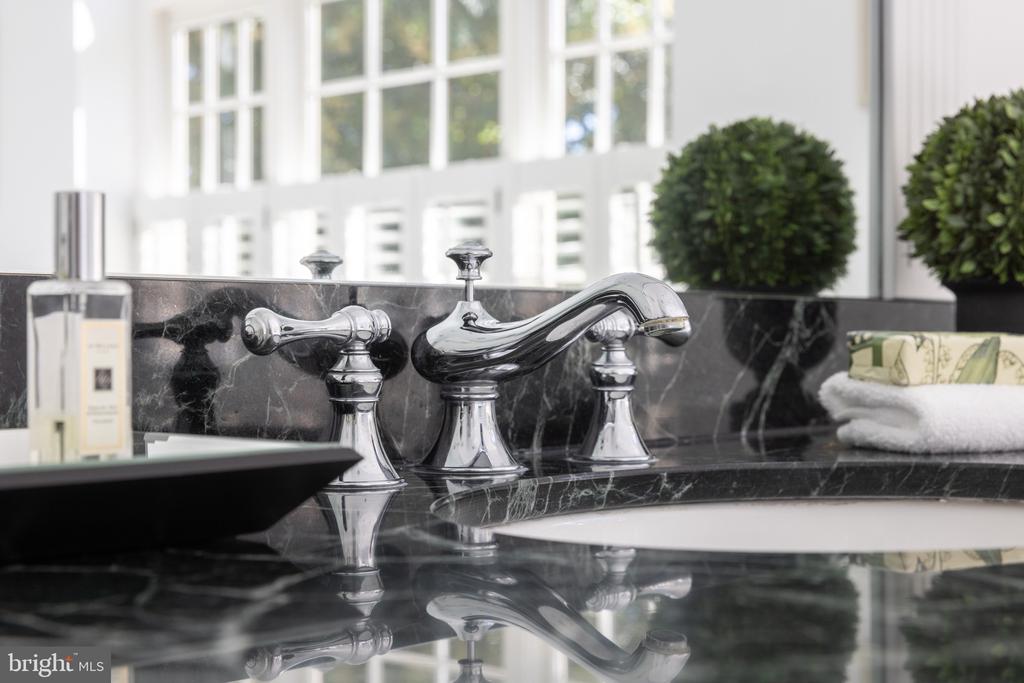 Bathroom vanity with polished chrome faucet, dark marble counter and backsplash, and white sink.