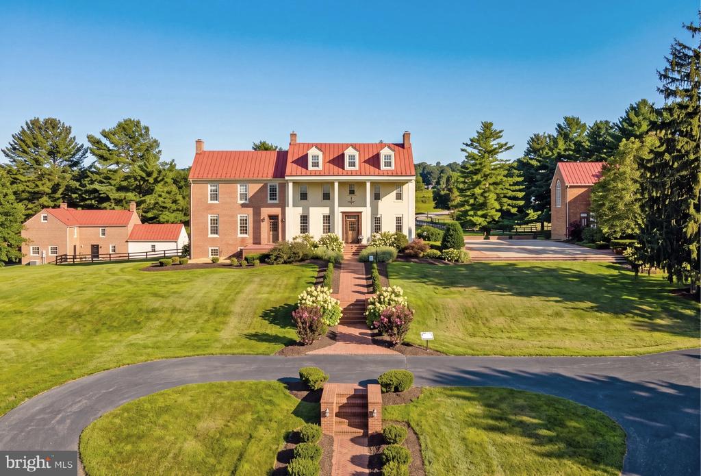 Brick Colonial home with a red metal roof, landscaped grounds, and two outbuildings.