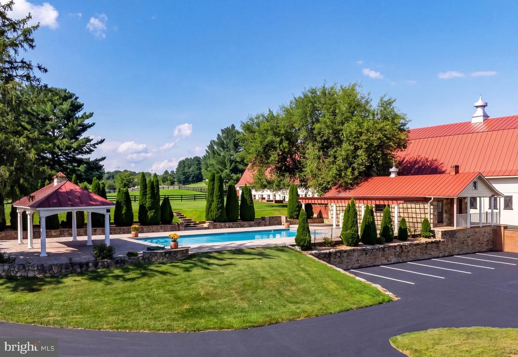 Red-roofed property buildings beside a swimming pool and gazebo, with landscaped grounds and paved parking.