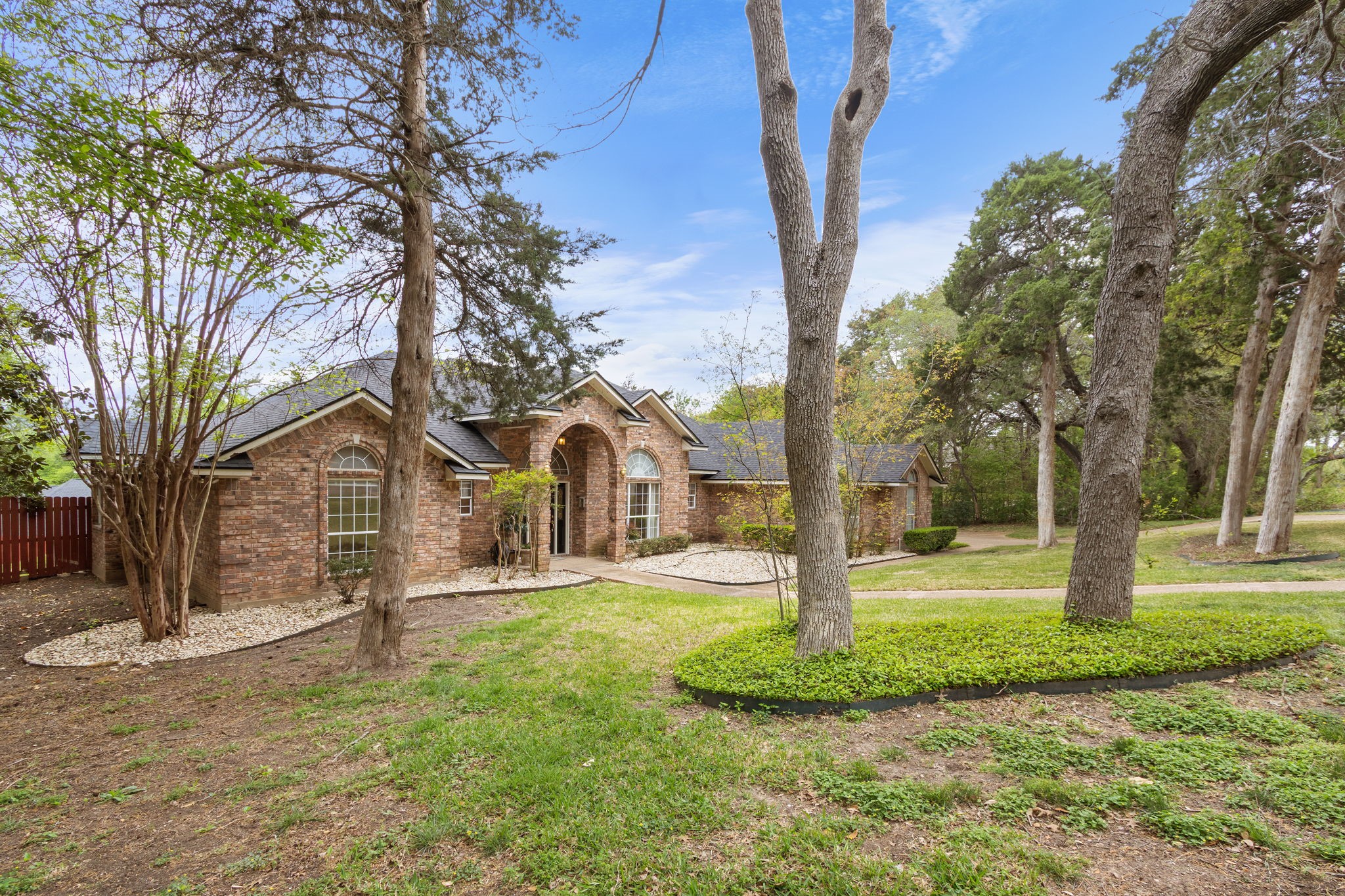Brick house with an arched entry and windows, framed by mature trees and a landscaped front lawn.