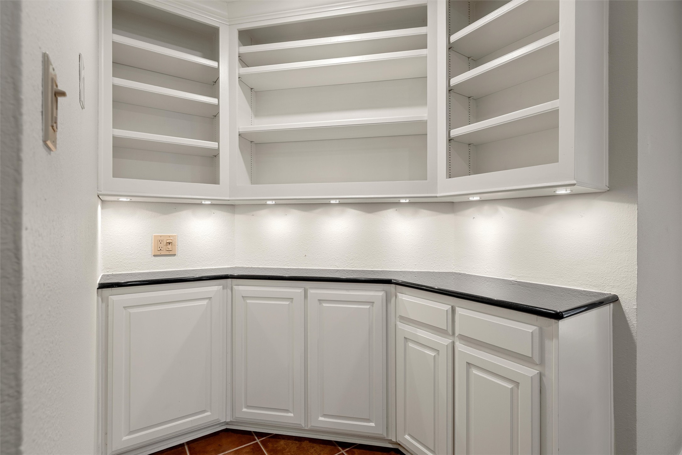 White built-in corner cabinets with open shelves, under-cabinet lights, and dark countertops.