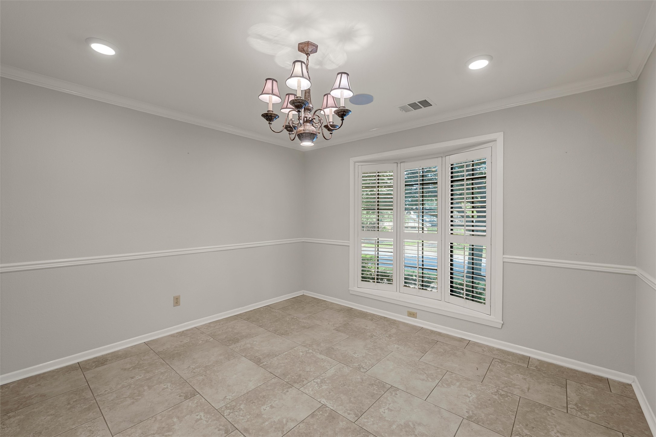 Empty tiled room with plantation-shuttered windows and a decorative chandelier.