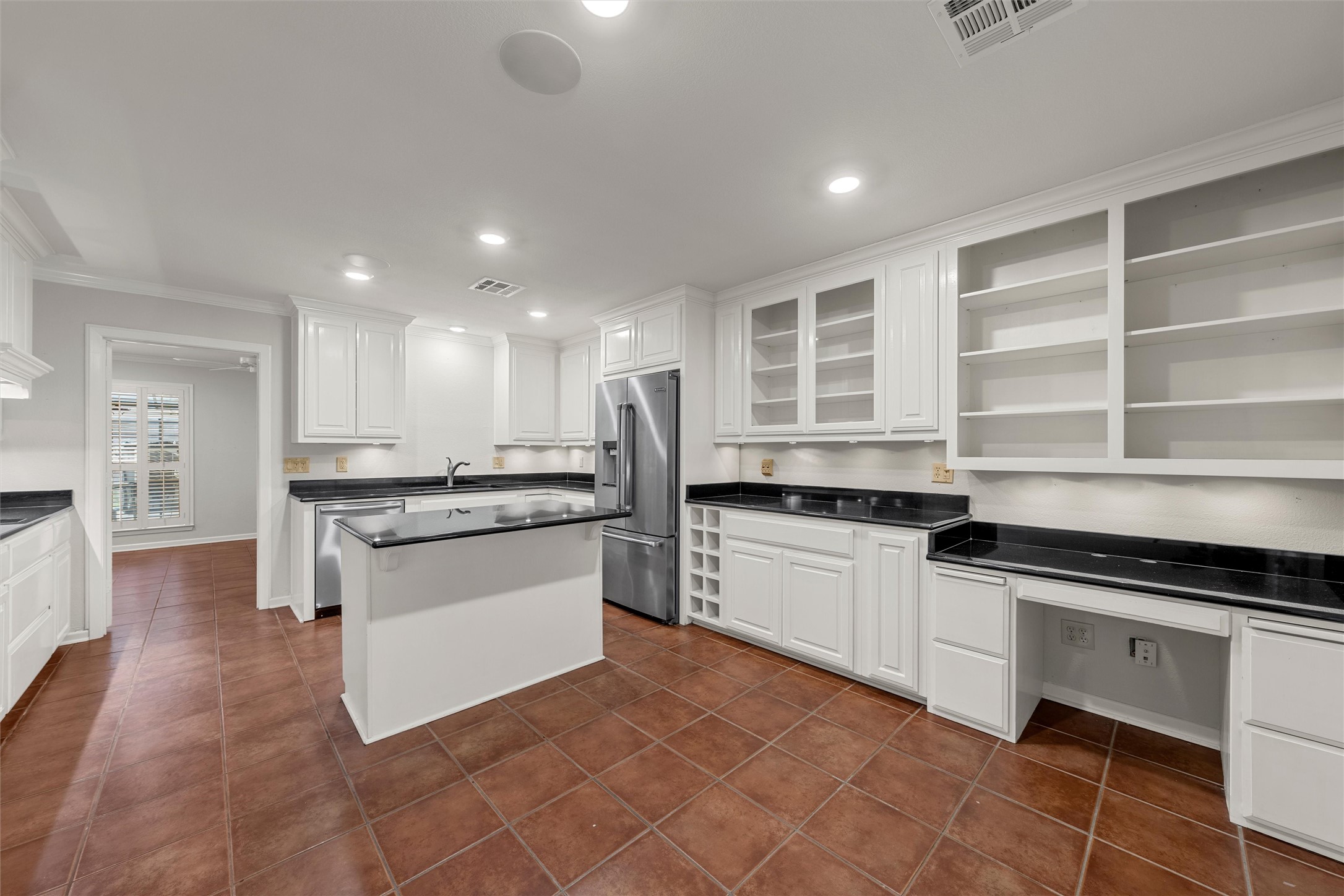 Kitchen with white cabinetry, black countertops, a central island, and terracotta tile floors.
