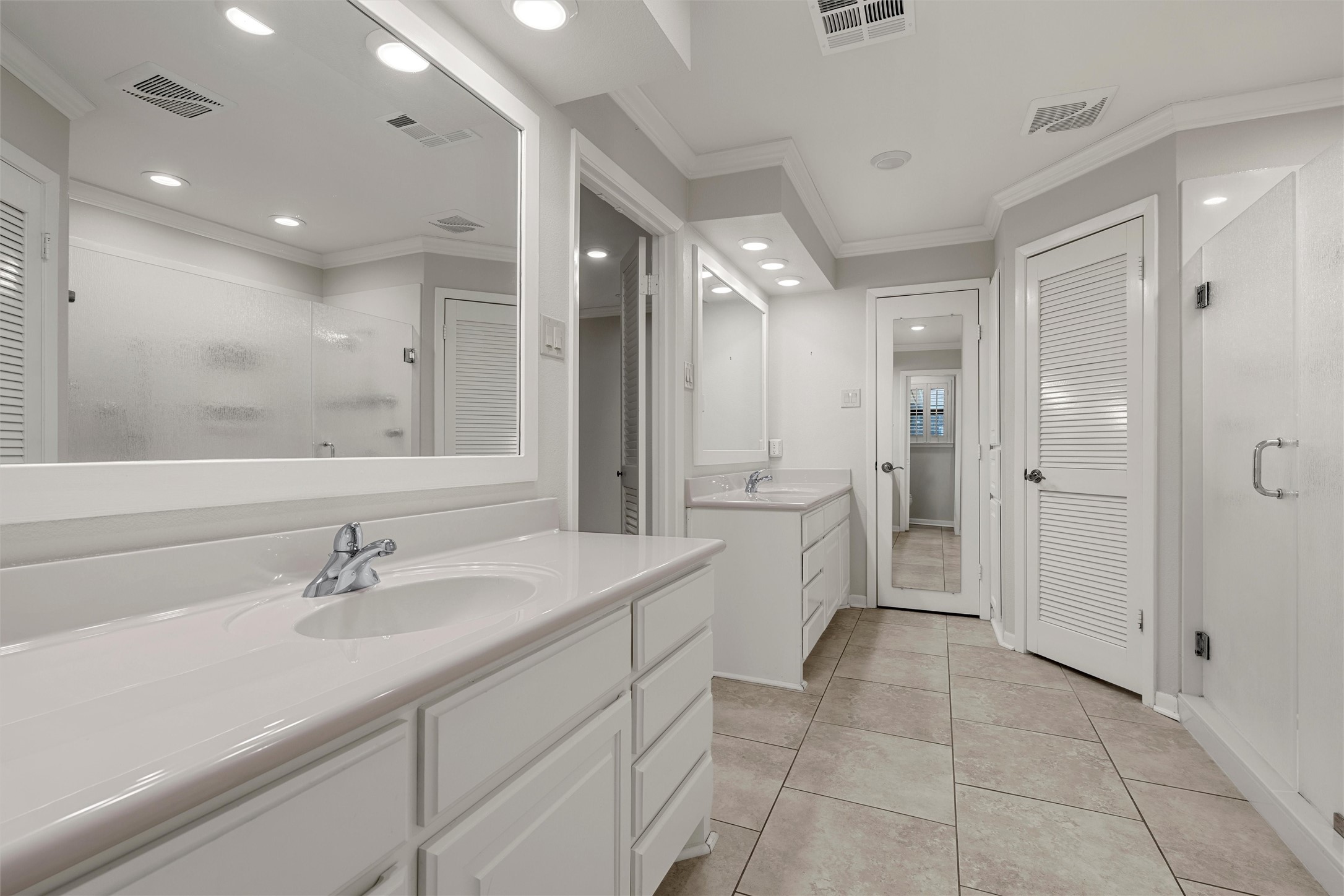 Bathroom with a long white double vanity, large mirrors, and beige tiled floor.
