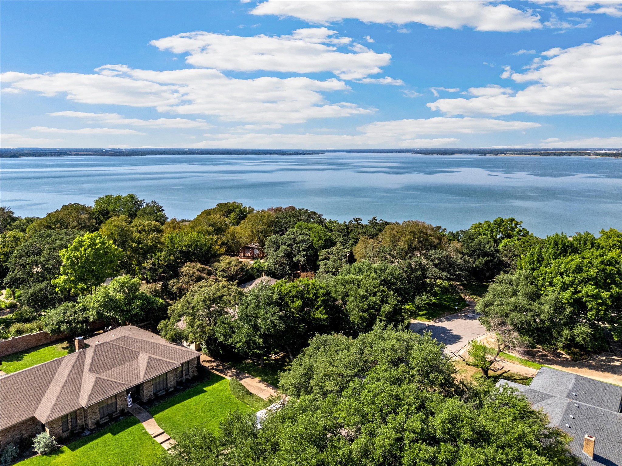 Aerial view of tree-shaded homes beside a broad lake under a partly cloudy sky.