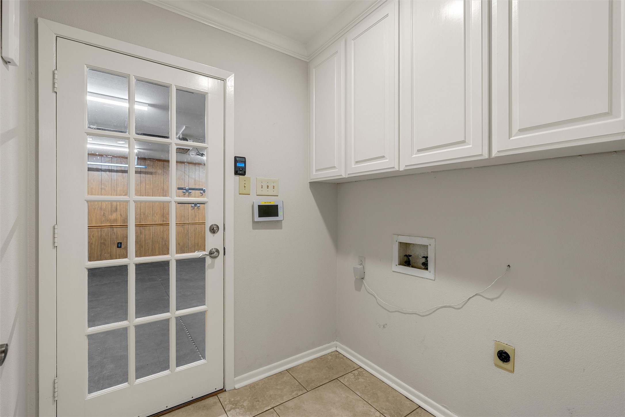 Laundry area with white cabinets, tiled floor, and a glass-paneled door beside the hookups.