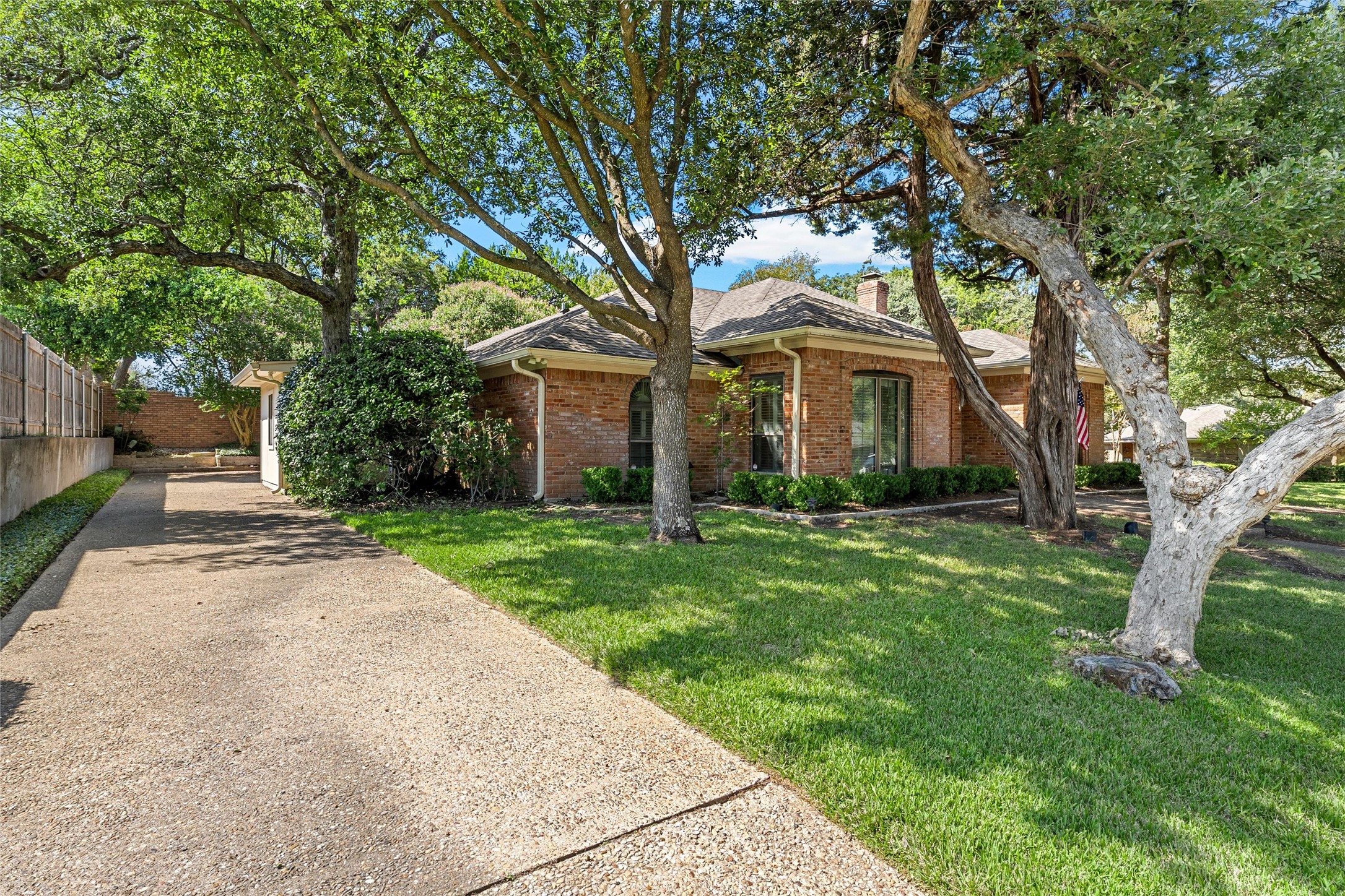 Red brick house framed by mature shade trees, with a broad driveway and green front lawn.