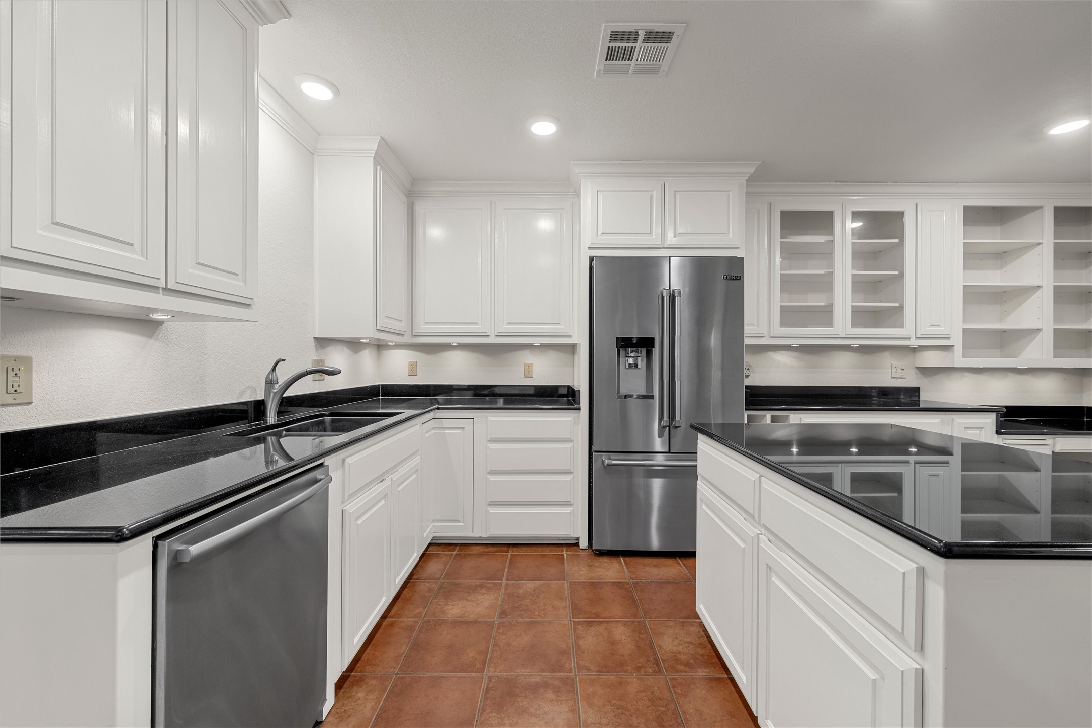 Kitchen with white cabinets, black countertops, stainless steel appliances, and reddish-brown tile flooring.