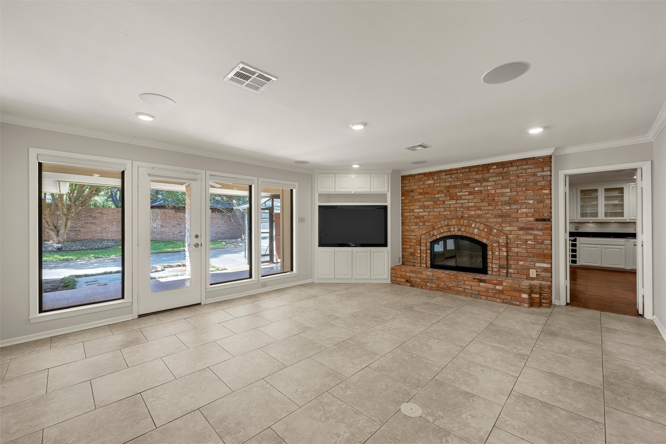 Living room with a brick fireplace, built-in television cabinetry, and wide windows and glass doors.