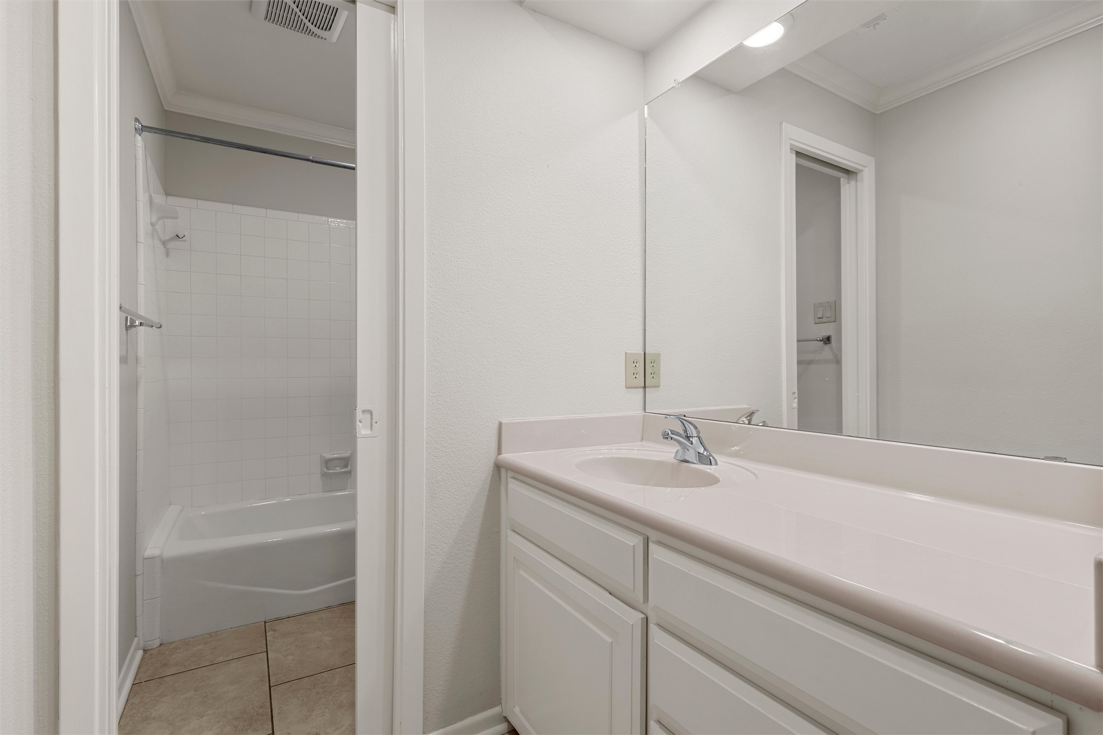 Bathroom with a long white vanity and mirrored wall beside a tiled tub and shower.