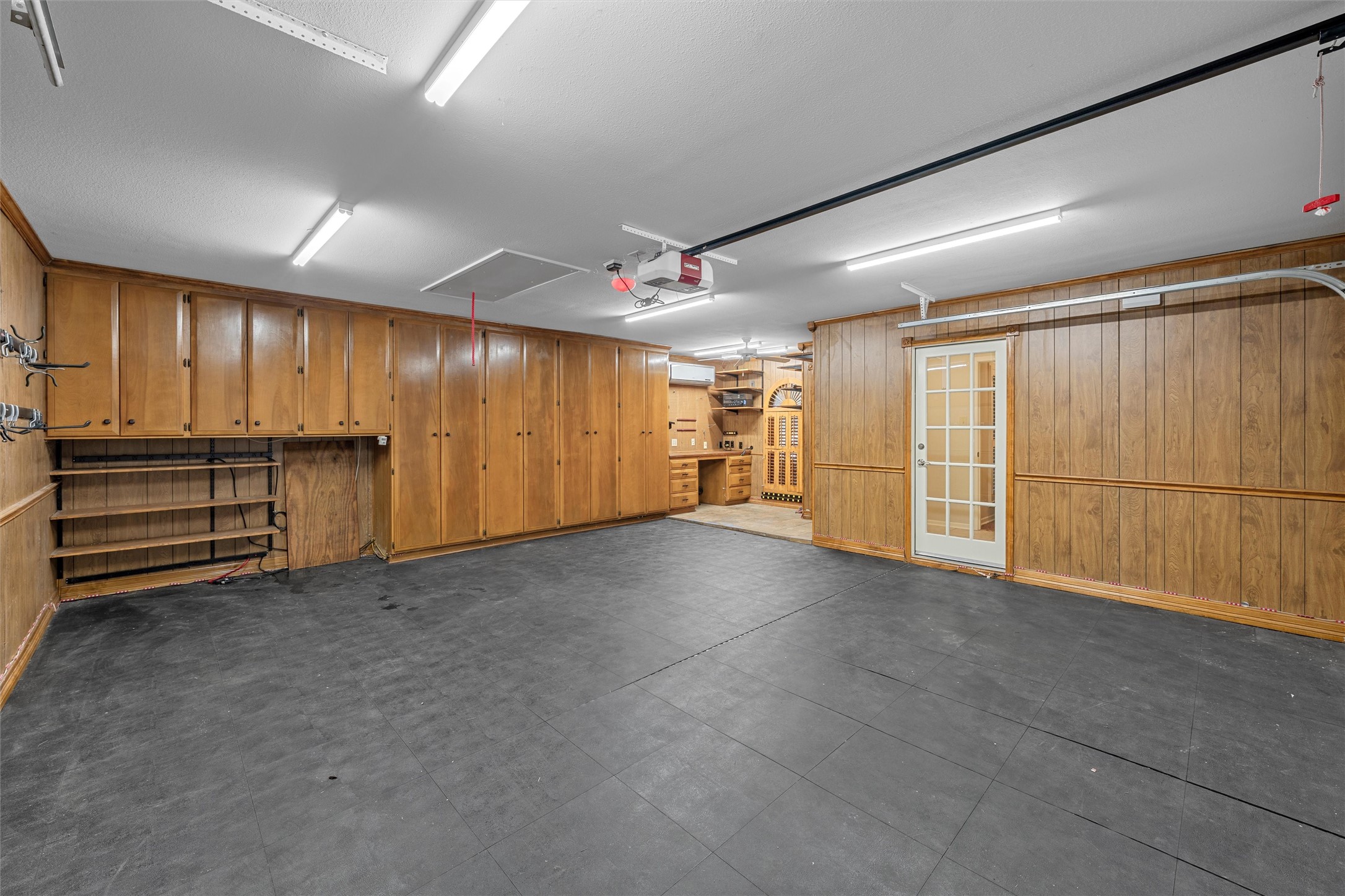 Garage with dark tiled flooring, extensive wood cabinets, and a glass-paneled side door.