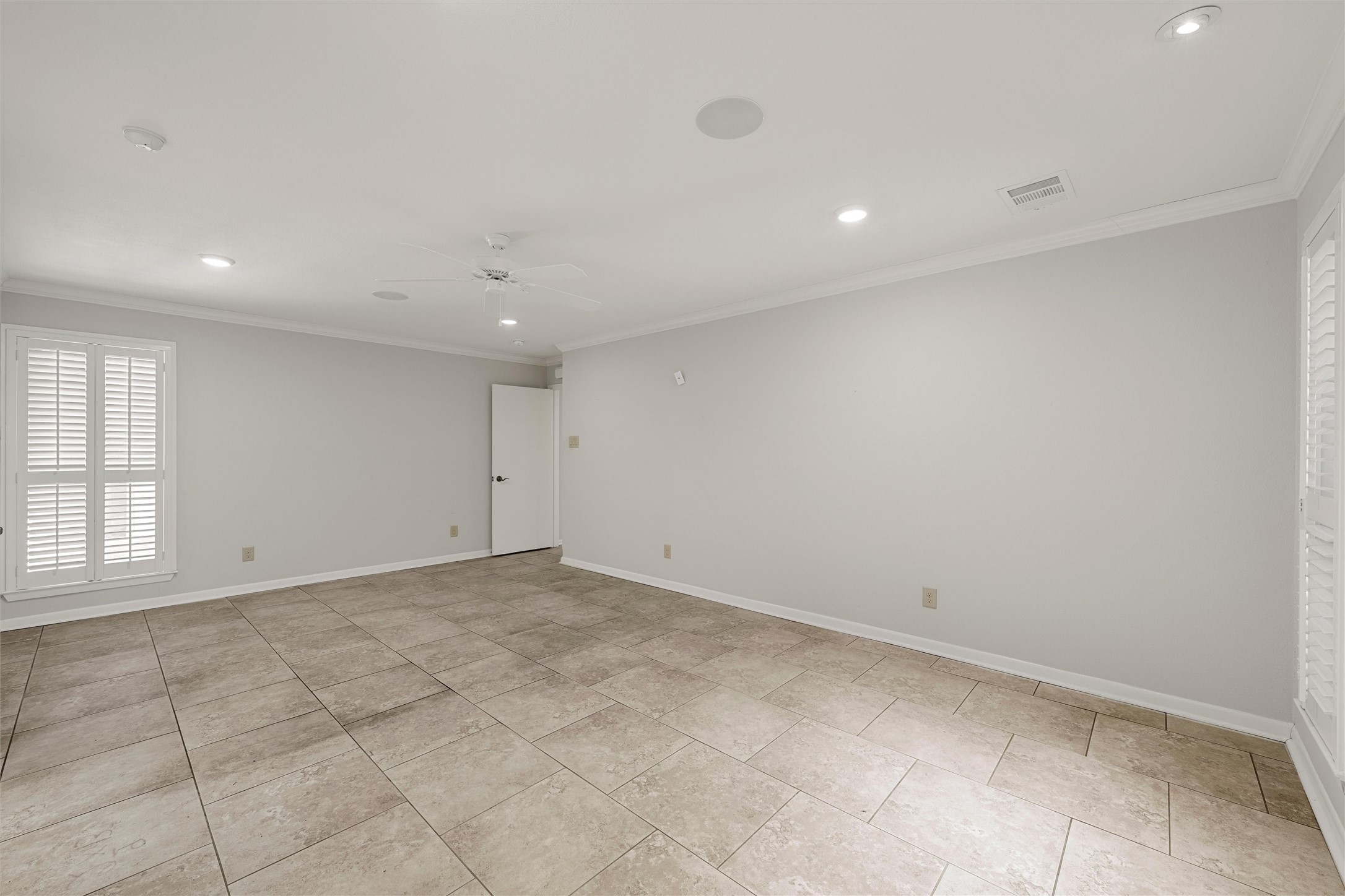 Empty room with large tile floors, plantation shutters, and a ceiling fan.