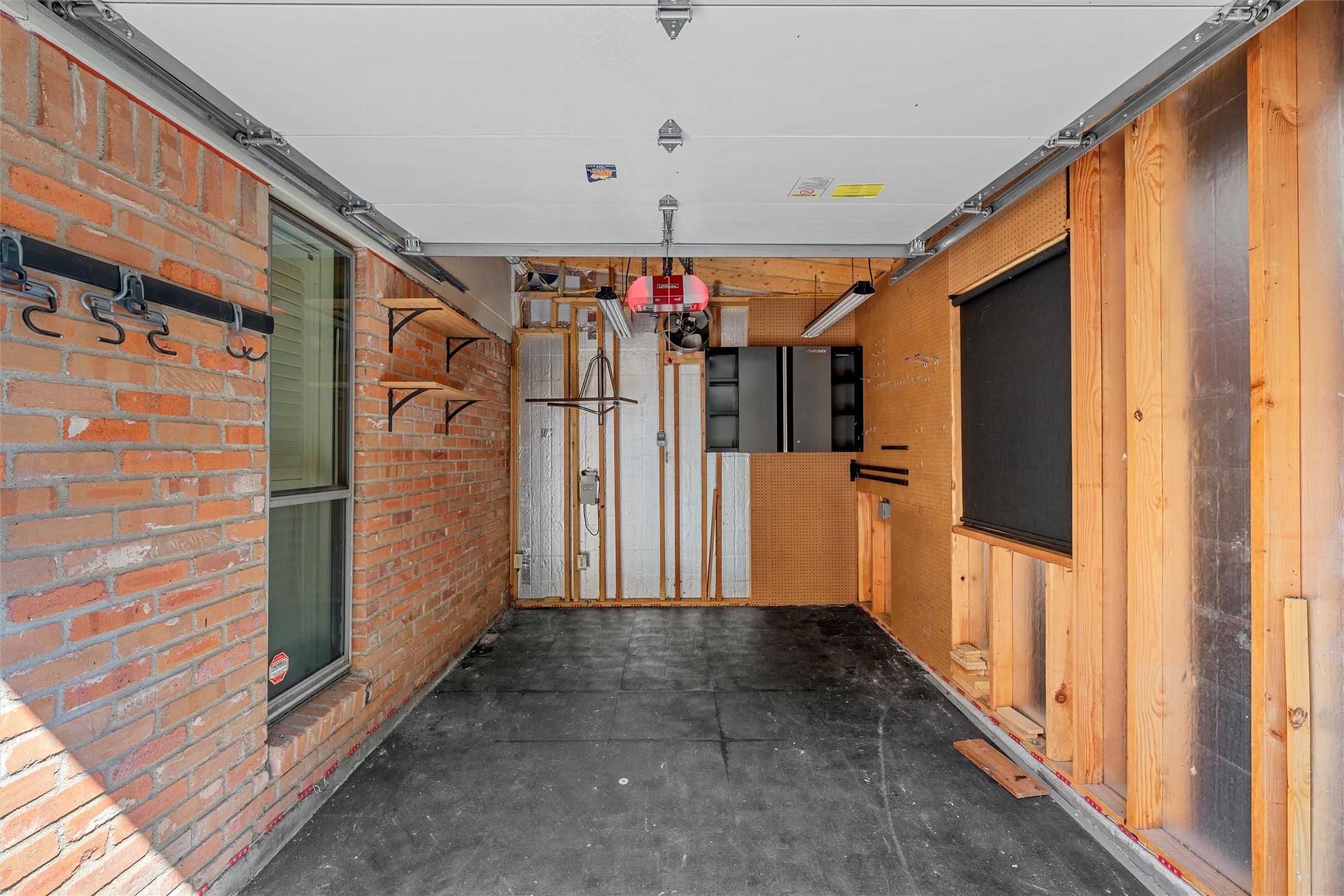 Garage interior with exposed brick, pegboard tool storage, and a ceiling-mounted door opener.