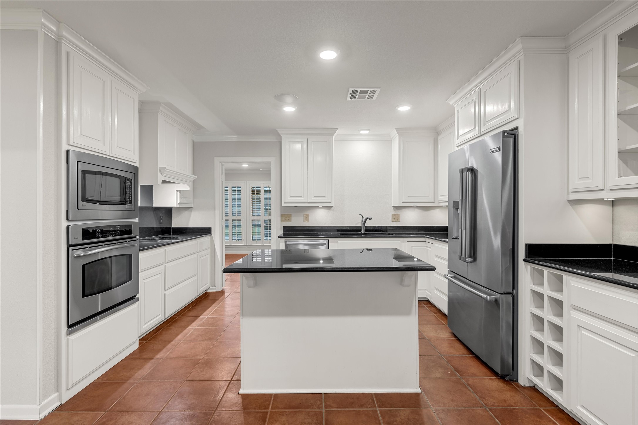 Kitchen with white cabinets, black countertops, stainless appliances, and a central island.