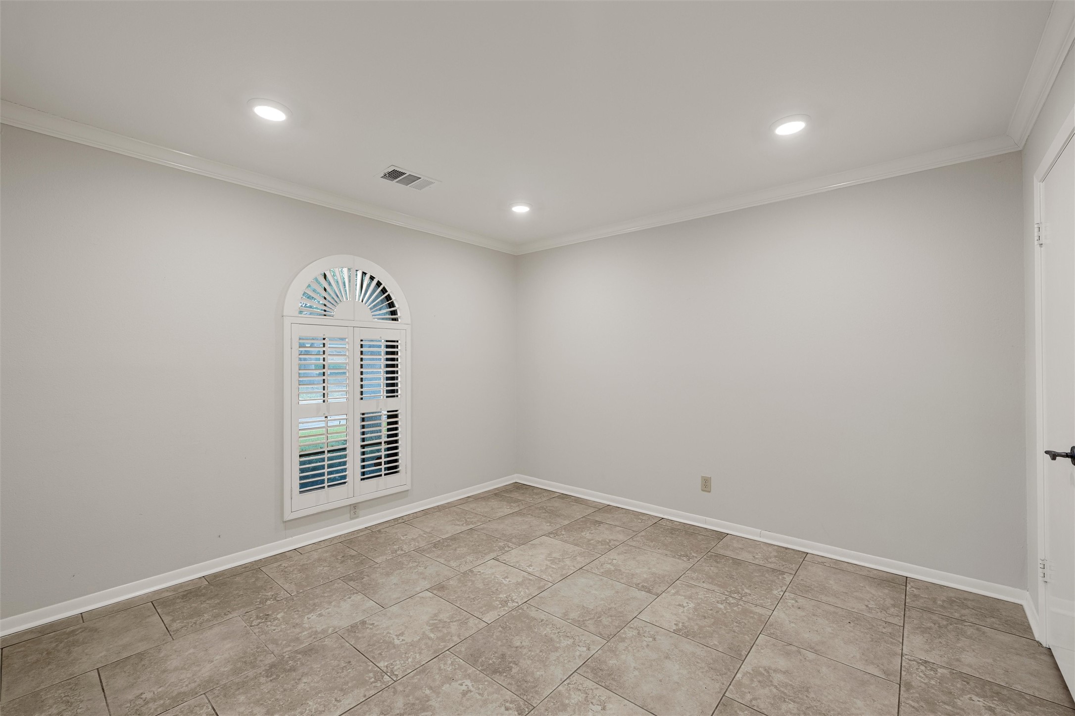 Empty room with tiled floors and an arched plantation-shuttered window.
