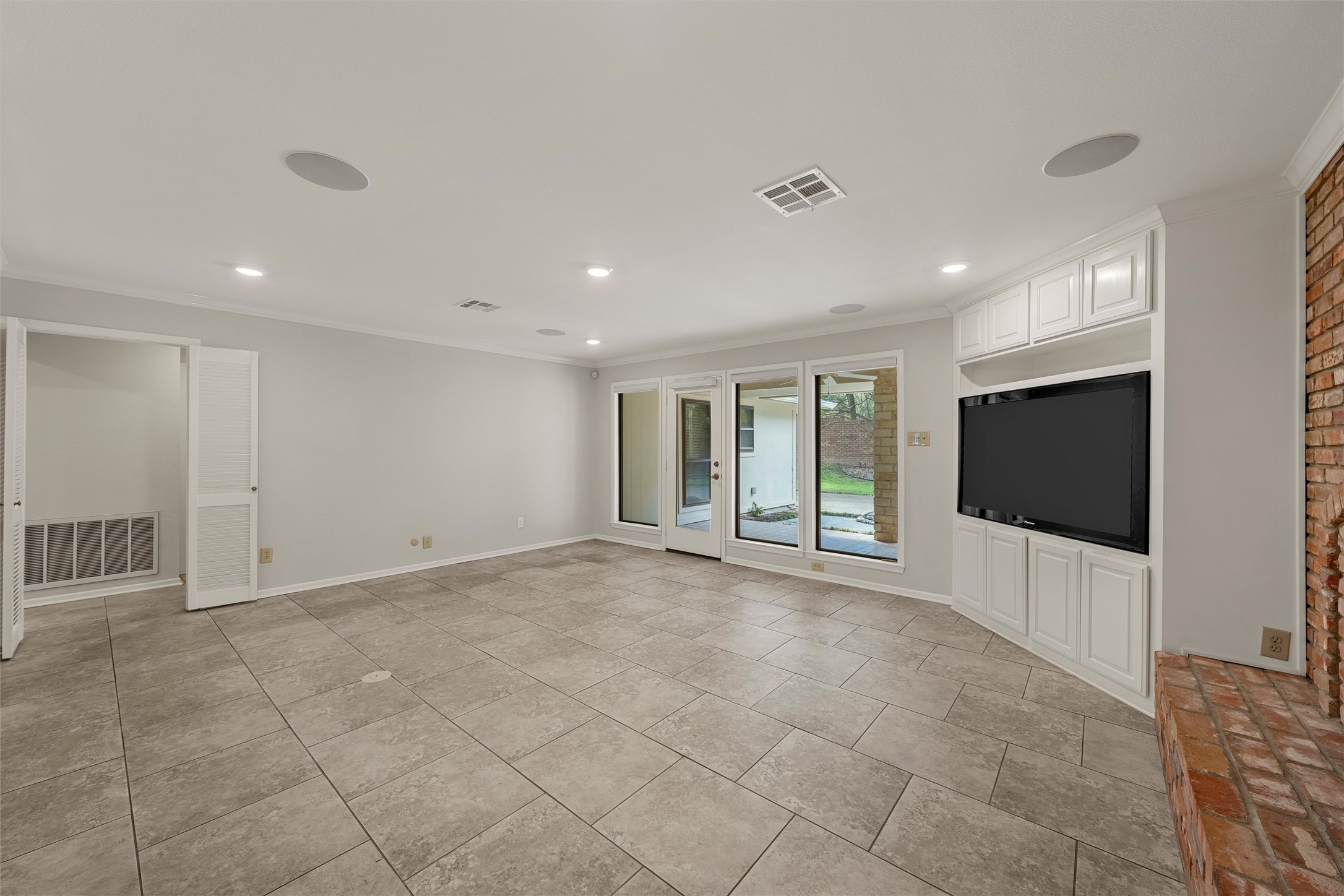Empty living room with gray tile floors, built-in TV cabinet, brick hearth, and glass doors to the yard.