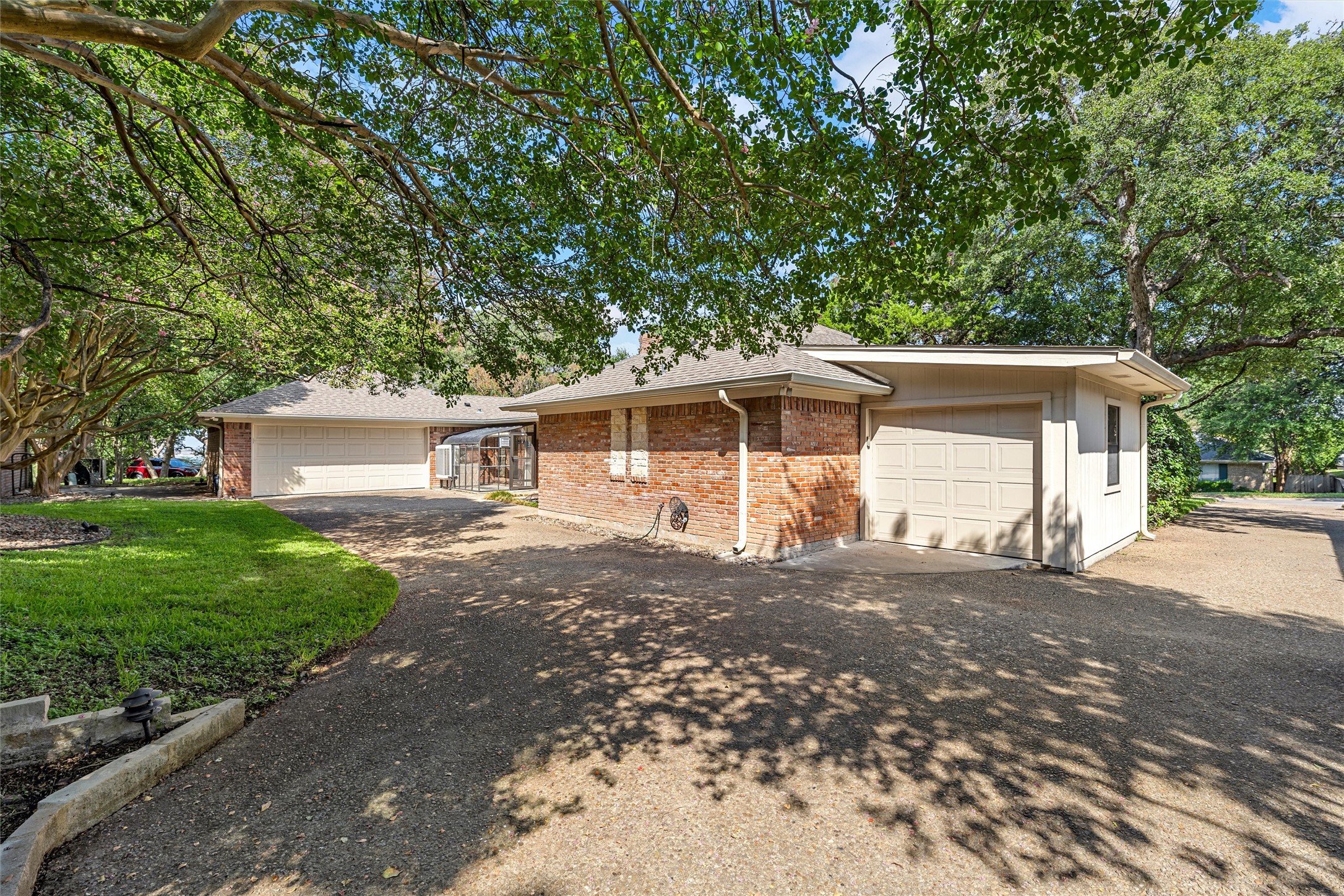 Brick home with two garages and a wide driveway shaded by mature trees.