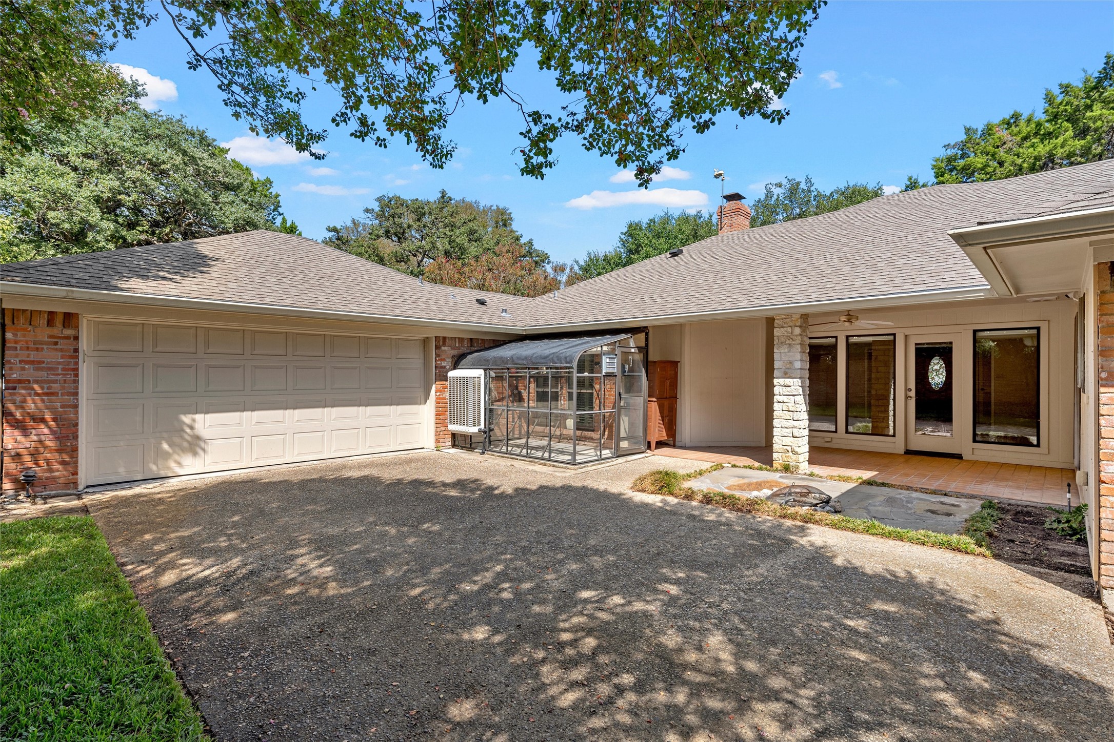 Rear exterior with a two-car garage, covered patio, and greenhouse beside the driveway.