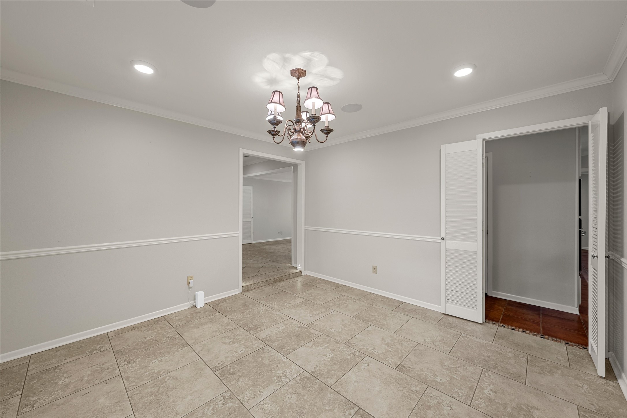 Empty tiled dining room with a chandelier, chair rail, and open louvered doors.