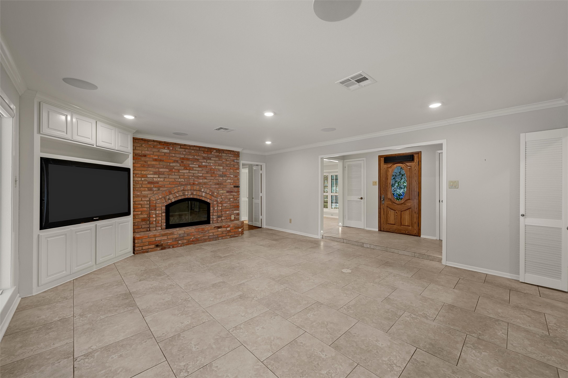 Living room with a brick fireplace, built-in television cabinetry, tiled floors, and a carved wooden entry door.