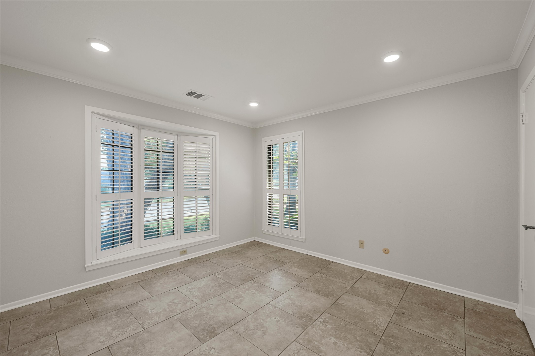Empty room with large shuttered windows and beige tile flooring.