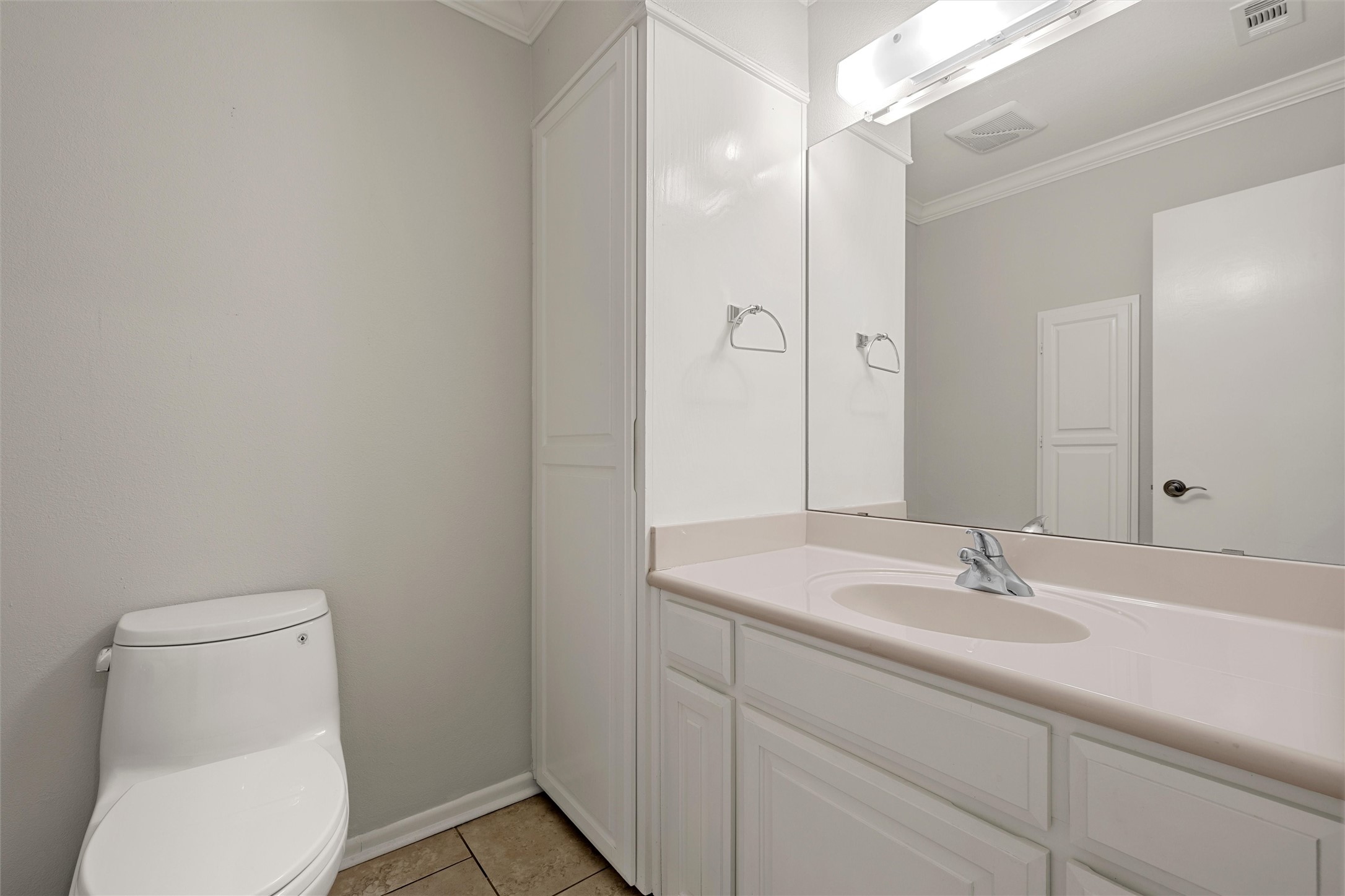 Bathroom with a white vanity, large mirror, built-in cabinets, and toilet.