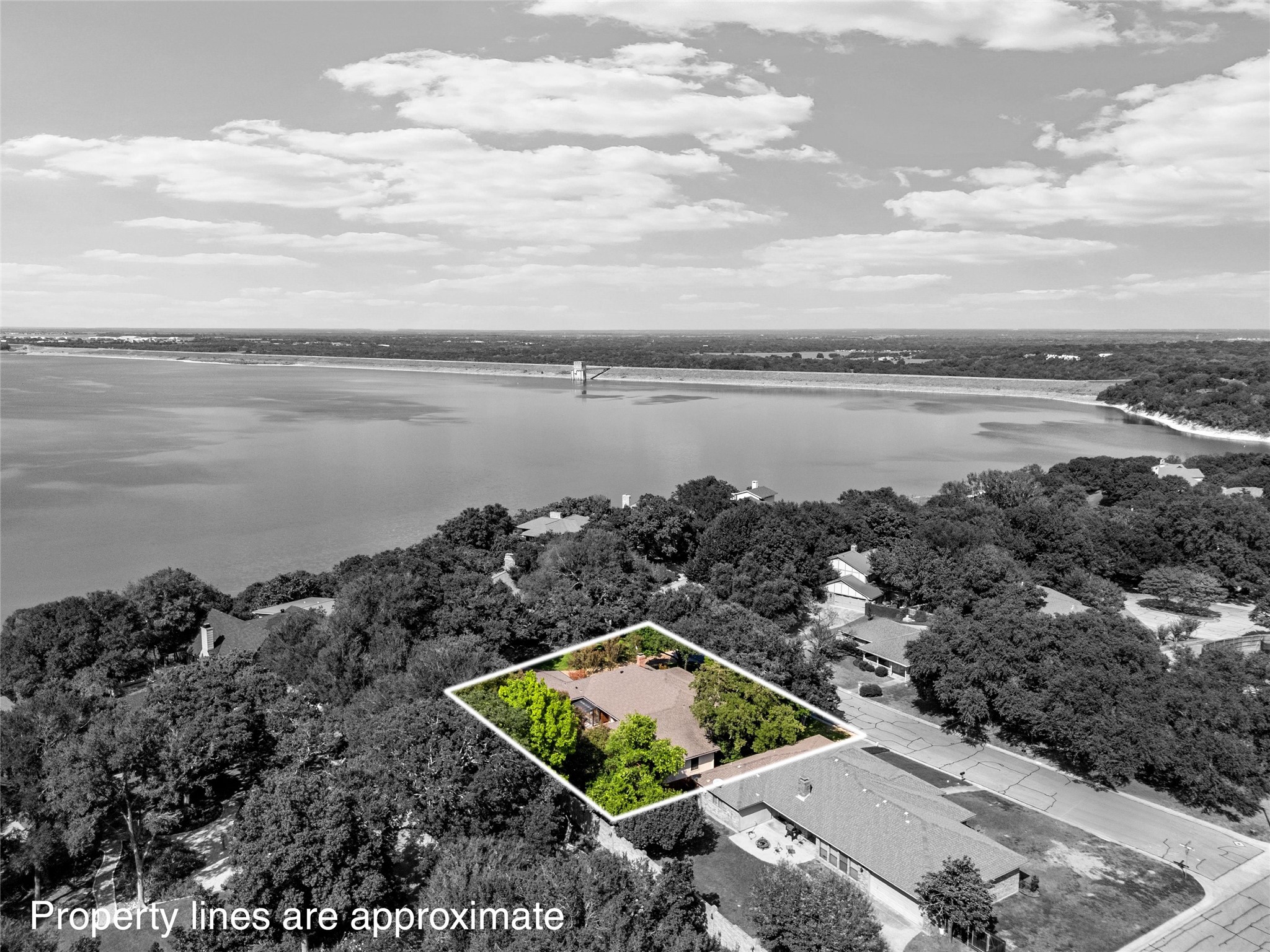 Aerial view of the outlined home and wooded lot, with a large lake beyond the neighborhood.