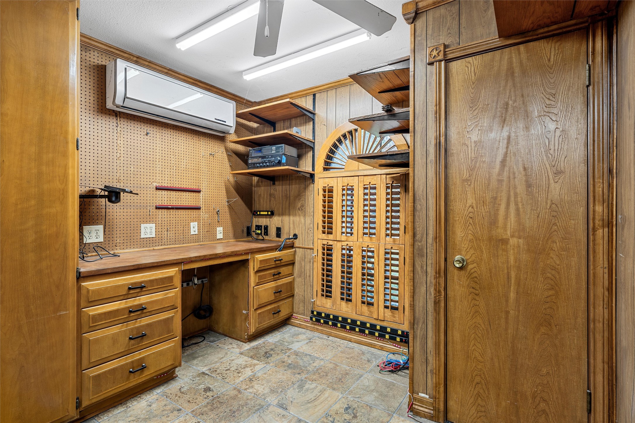 Wood-paneled workshop with a built-in workbench, pegboard wall, and extensive cabinetry.