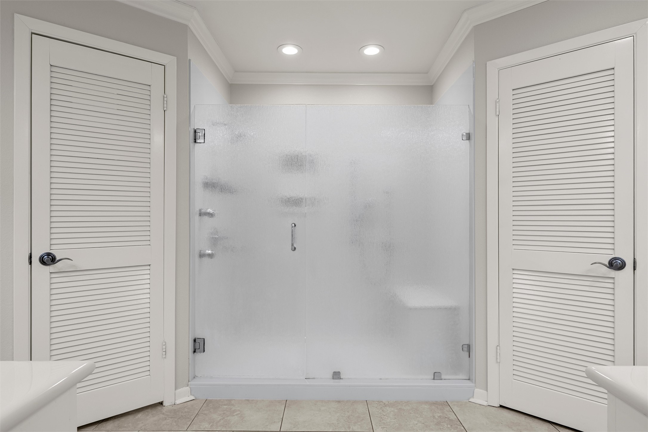 Bathroom walk-in shower with frosted glass doors, chrome hardware, and white louvered doors on either side.