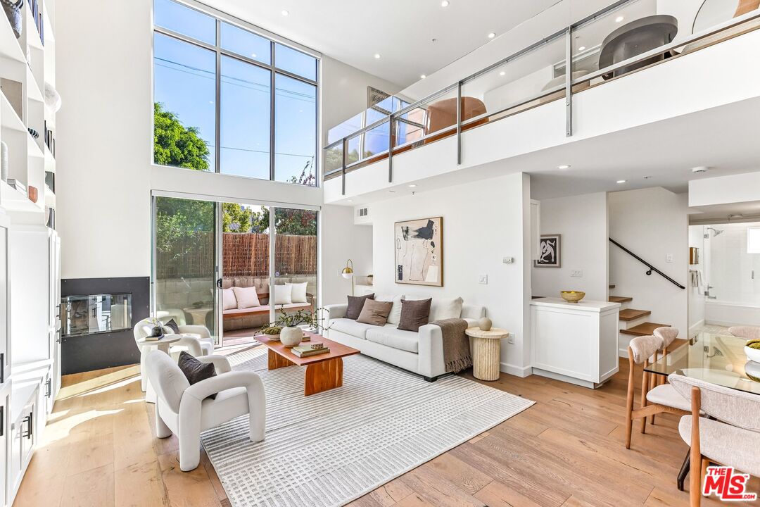 Double-height living room with tall windows, a modern fireplace, and glass doors opening to a patio.