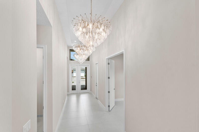 Bright entry hallway with white tile floors, high ceilings, and two crystal chandeliers.