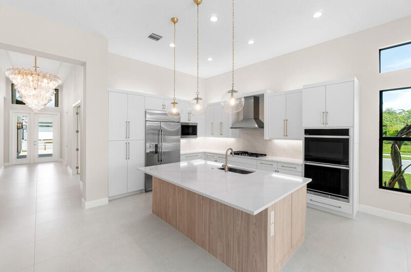 Modern kitchen with a large wood-front island, white cabinets, and stainless steel appliances.
