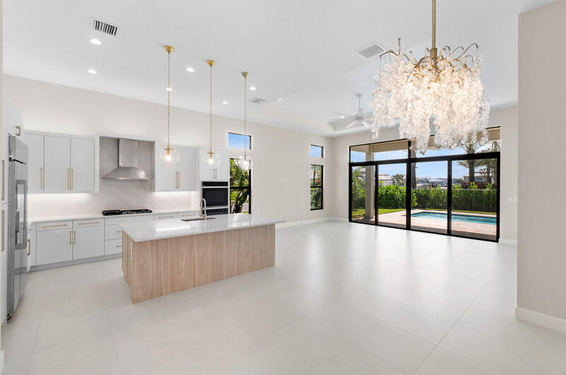 Open kitchen with a wood-front island and chandelier beside sliding doors overlooking a pool.