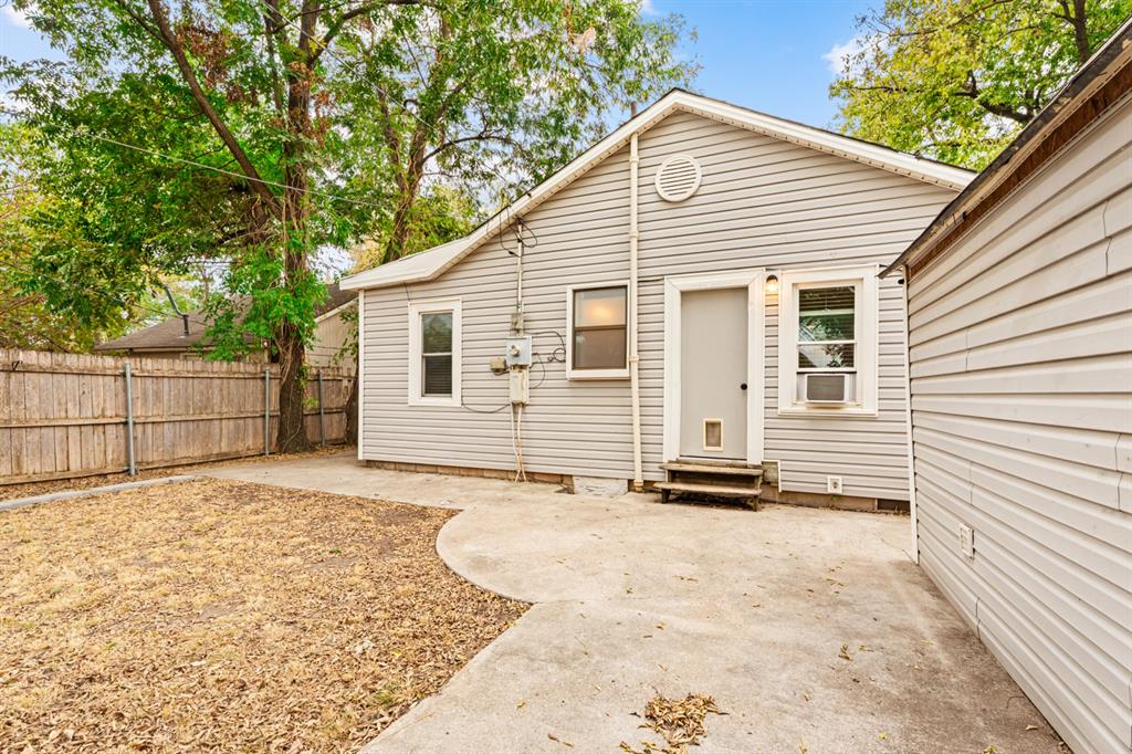 Rear of a light-sided home with a concrete patio, fenced yard, and mature trees.