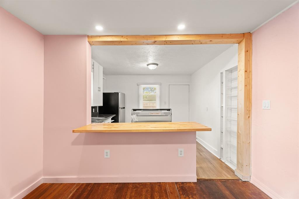 Kitchen with a wood pass-through counter, white cabinets, black appliances, and adjoining pink walls.