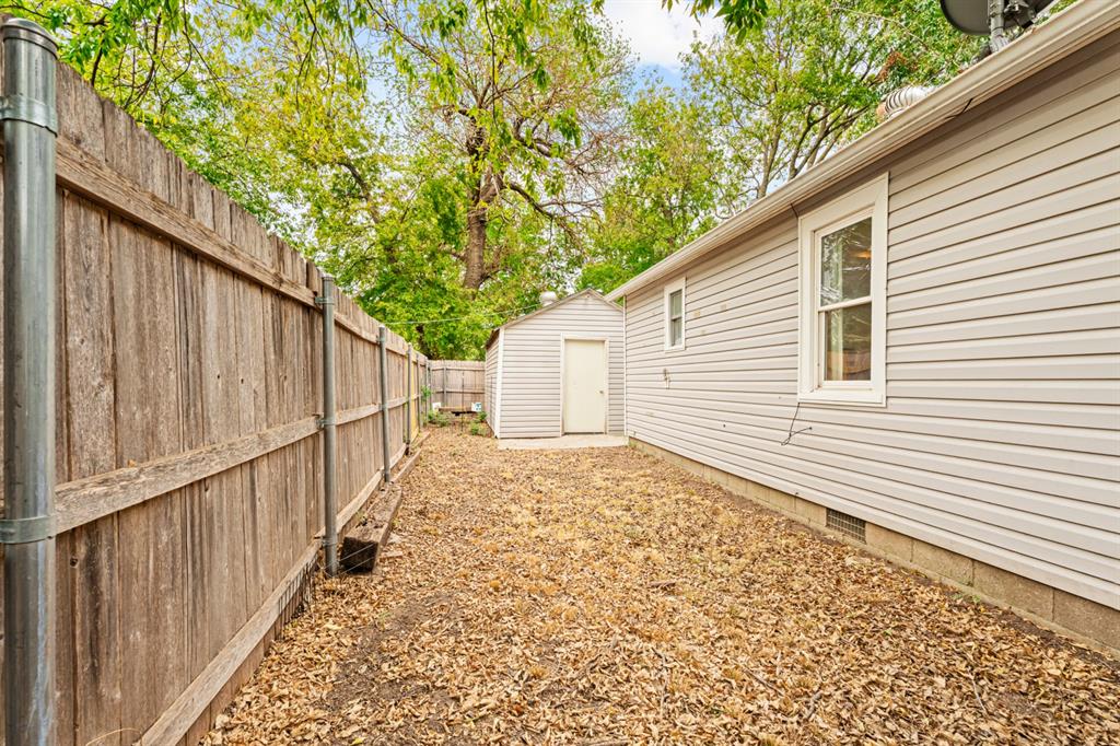 Side yard with a wooden privacy fence, leaf-covered ground, and a small storage shed.