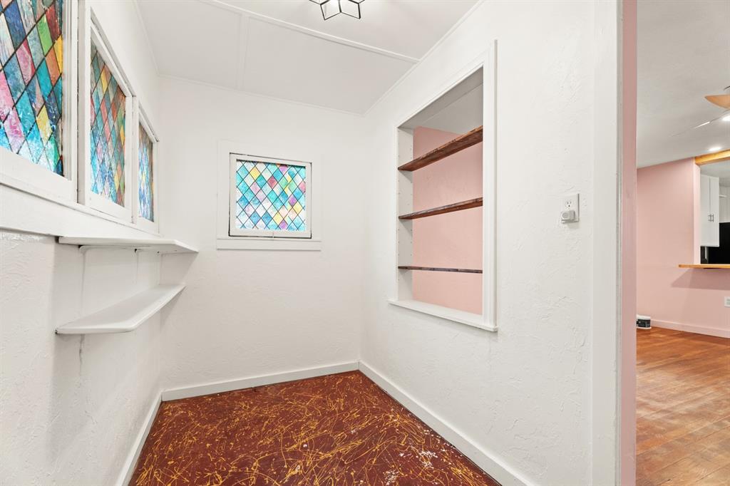 Small empty room with colorful stained-glass windows, built-in shelves, and a reddish-brown floor.