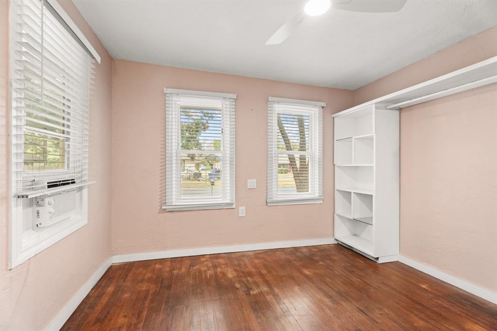 Empty bedroom with peach walls, hardwood floors, window air conditioner, and built-in white shelving.