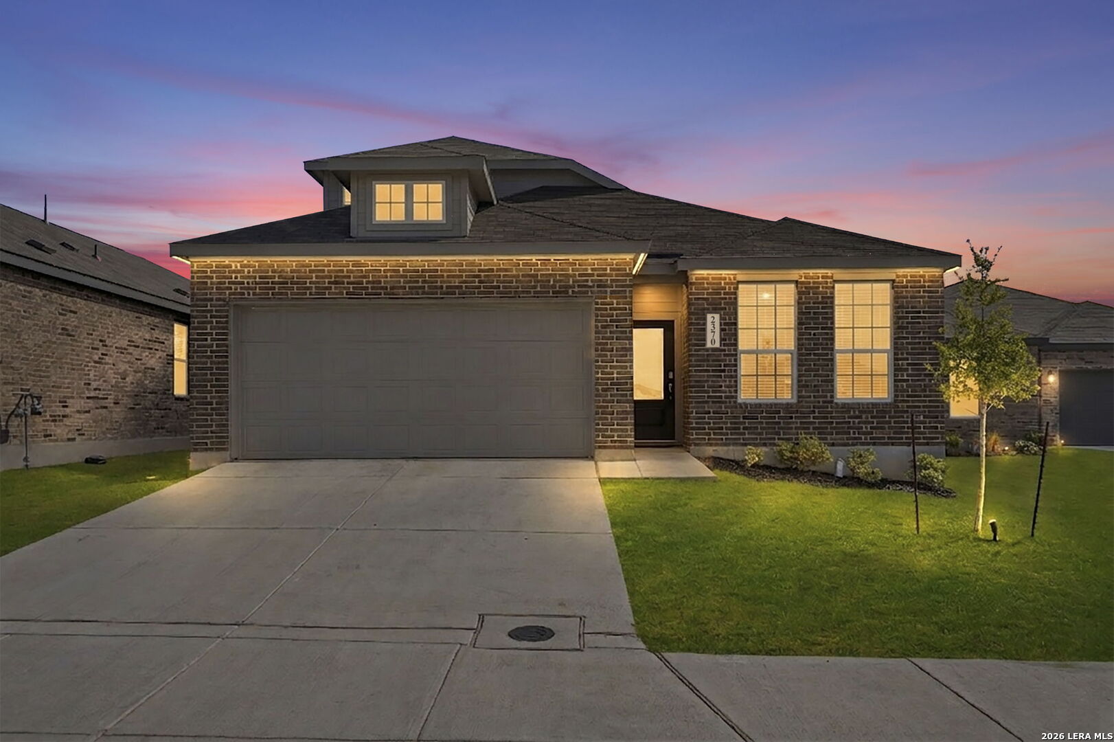 Brick home with a wide garage and glowing windows beneath a pink-and-blue dusk sky.