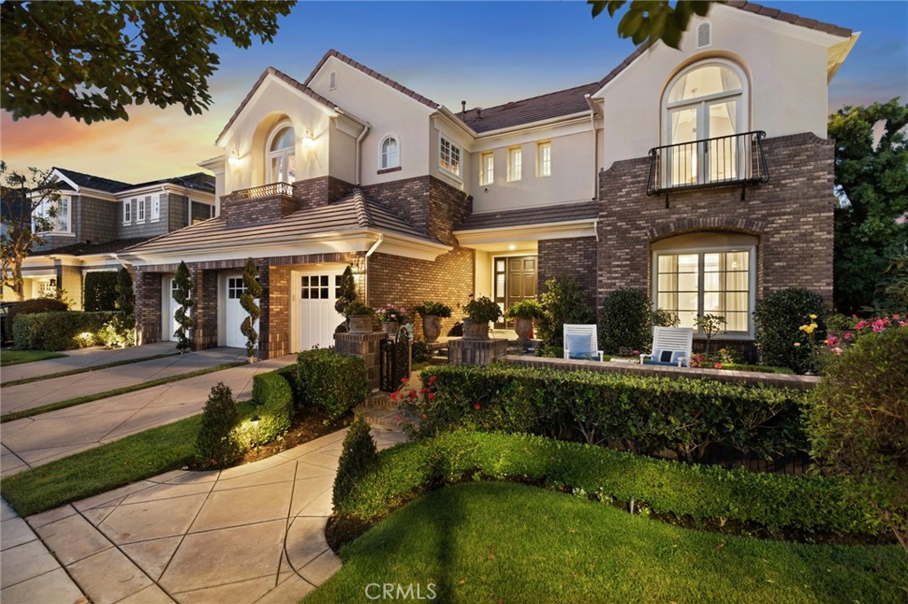 Two-story stucco and brick home with arched windows, balconies, and landscaped grounds at dusk.